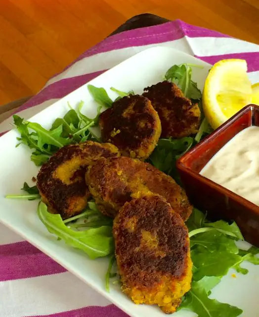 Golden-brown crab cakes served with a creamy dipping sauce and lemon wedge on greens.