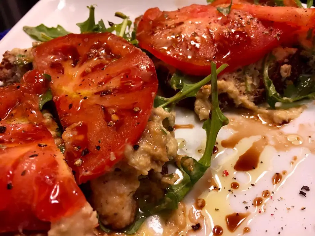 Grilled tomato halves on a bed of greens with a drizzle of balsamic glaze.
