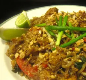A plate of spicy crab dish garnished with green onions and lime wedges.