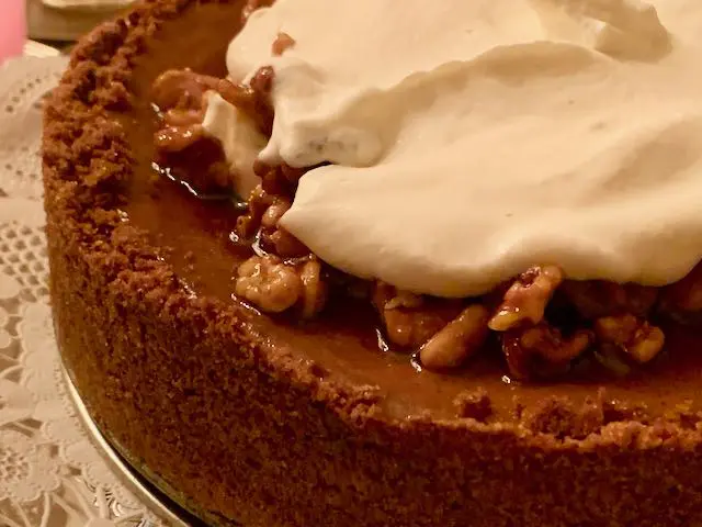Close-up of a rich caramel cake topped with whipped cream and nuts.