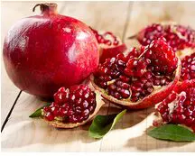Fresh pomegranates with seeds spilling out on a wooden surface.