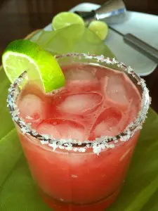 A refreshing pink cocktail with ice, lime wedge, and salt rim.