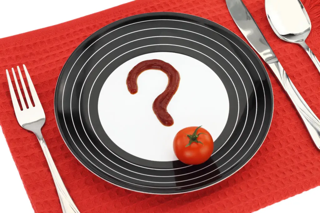 Tomato with ketchup shaped like a question mark on a plate.