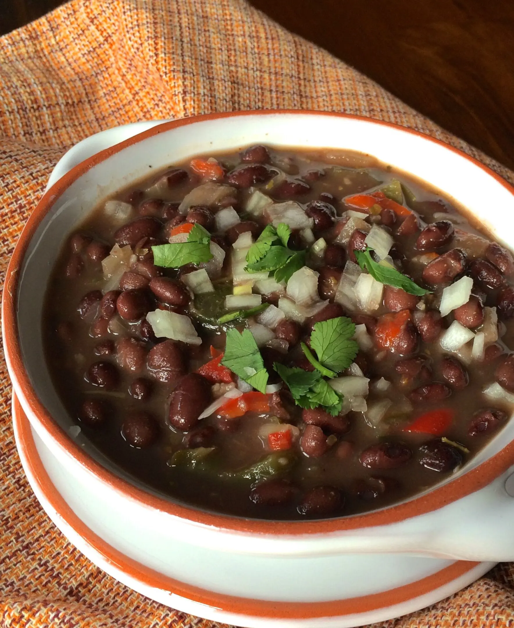 A bowl of black bean soup garnished with fresh herbs and diced onions.