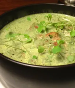 Creamy green soup garnished with fresh herbs in a dark bowl.