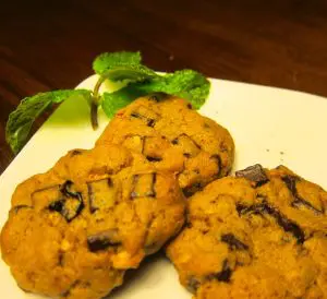 Two chocolate chip cookies on a white plate with a mint garnish.