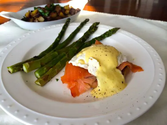 Eggs Benedict with smoked salmon and asparagus spears on a white plate.