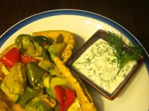 Plate of vegetable curry with a side of creamy herb sauce.