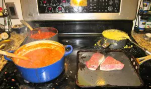 Cooking red snapper fillets, rice, and tomato sauce on stovetop burners.