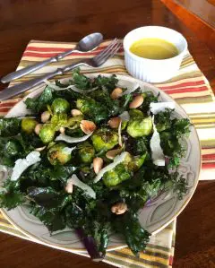 Plate of roasted Brussels sprouts with nuts and greens, served with a yellow sauce.