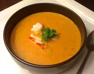 Creamy lobster bisque garnished with herbs in a black bowl.
