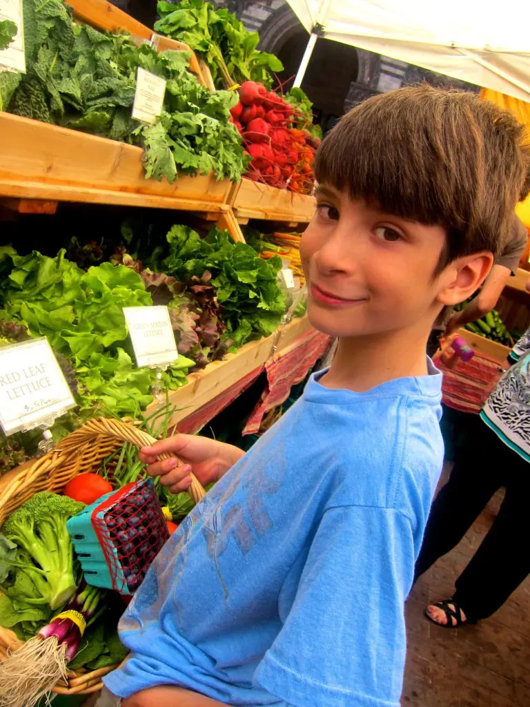 A smiling boy holding fresh produce at a market.
