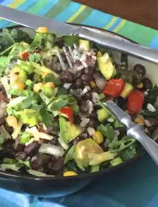 A colorful bowl of mixed bean salad with avocado and tomatoes.