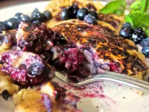 Close-up of a blueberry pancake with syrup and fresh blueberries.