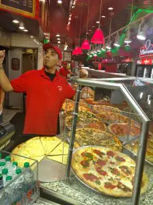 Pizza chef joyfully serving fresh pizzas behind the counter.