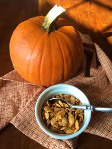 A pumpkin and a bowl of roasted pumpkin seeds on a cloth.