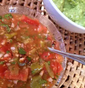 A bowl of fresh salsa with a spoon and a green dip in the background.