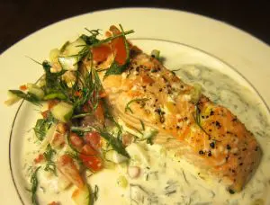 Grilled salmon topped with herbs and served with creamy sauce and vegetables.