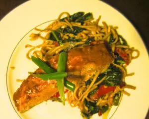 A plate of stir-fried noodles with vegetables and a crab claw.