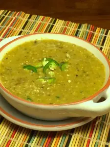 A bowl of thick green lentil soup garnished with green chili slices.