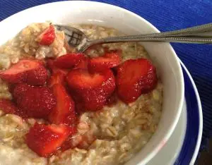 Bowl of oatmeal topped with sliced strawberries and a spoon.
