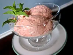 Two scoops of pink ice cream in a glass bowl with a mint garnish.