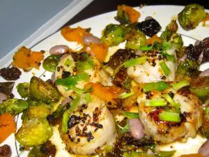 A colorful roasted vegetable and scallop dish with herbs and spices.