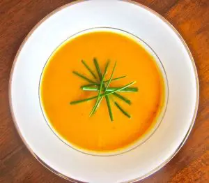 Creamy orange soup garnished with fresh green herbs in a white bowl.