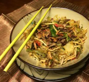 A bowl of stir-fried noodles with vegetables and yellow chopsticks.