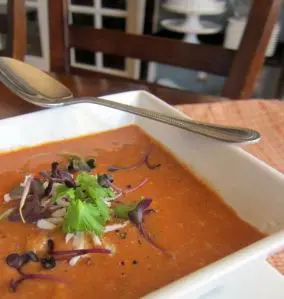 Creamy tomato soup garnished with herbs and microgreens.