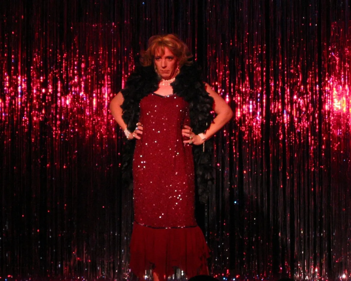 Performer in a sparkling red dress on stage with shimmering backdrop.