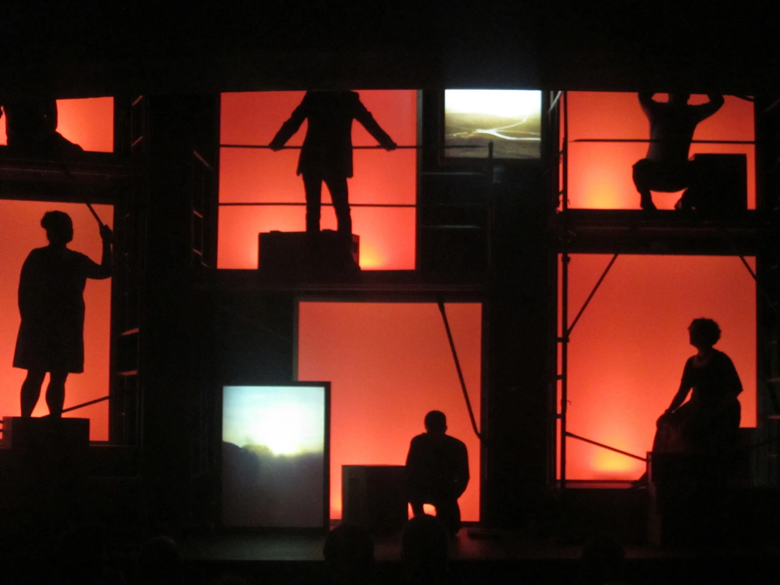 Silhouettes of people framed in window-like structures against a red background.