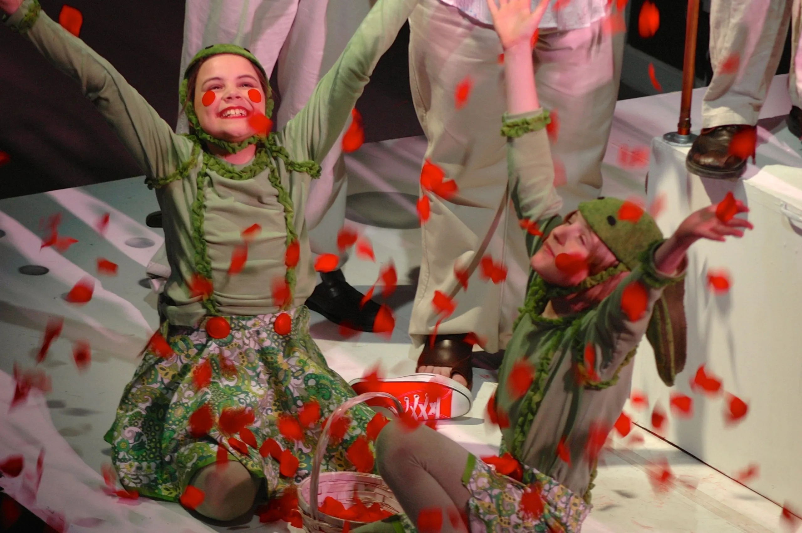 Dancers in green costumes with red floral patterns perform energetically on stage.