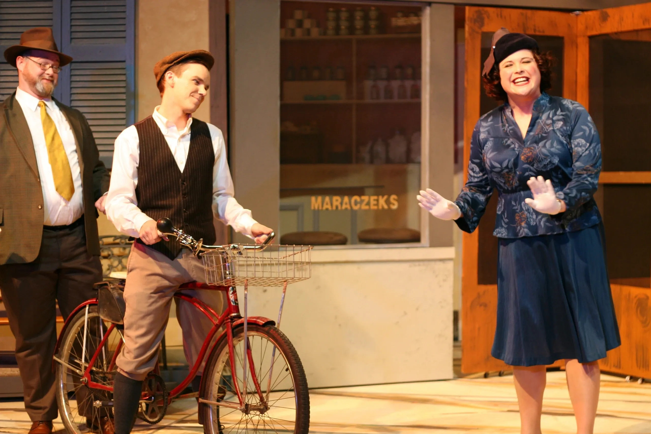 Actors performing a lively scene with a bicycle on stage.