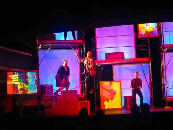 Actors performing on a colorful, illuminated stage at night.