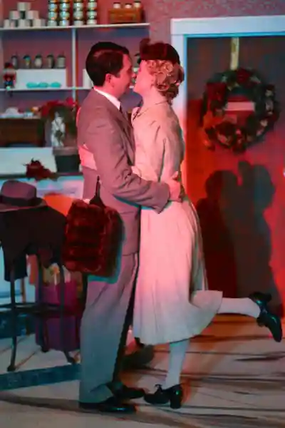 Couple dancing closely in a warmly lit room with holiday decorations.