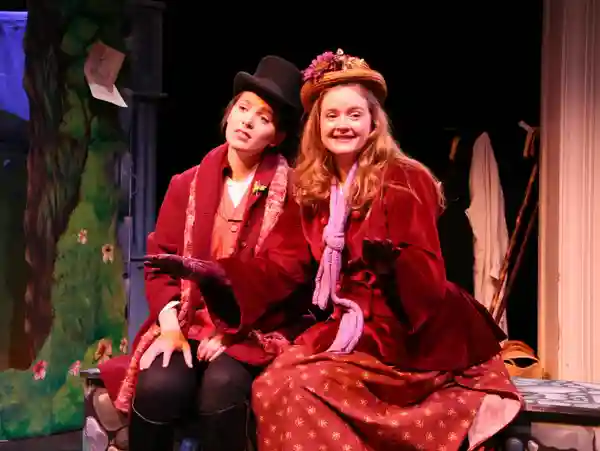 Two women in vintage costumes smiling during a theatrical performance.