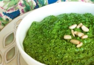 A bowl of green pesto garnished with pine nuts on a decorative plate.