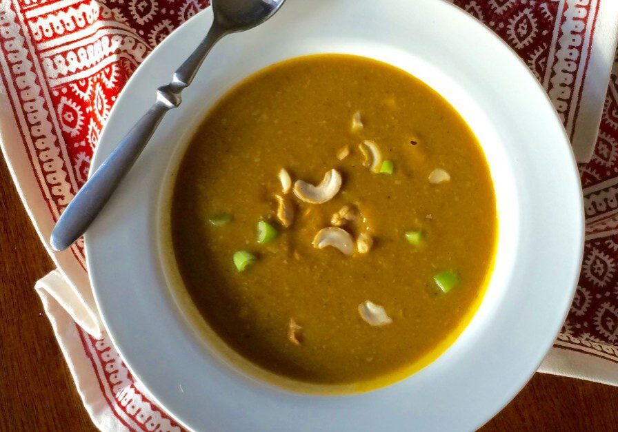 A bowl of creamy soup garnished with cashews and green herbs.