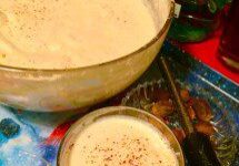 A bowl and glass filled with frothy, spiced beverage on a blue cloth.