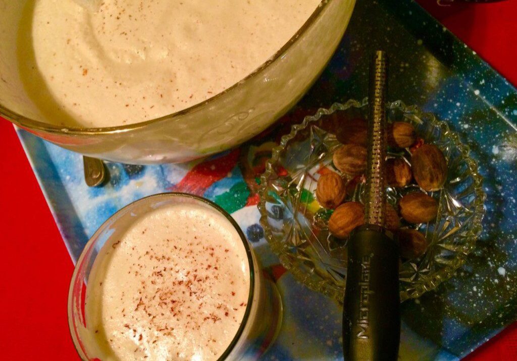 A glass of creamy beverage beside a bowl and a black knife on a colorful surface.