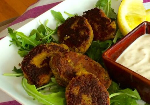 Golden-brown crab cakes served with a creamy dipping sauce and lemon wedge on greens.