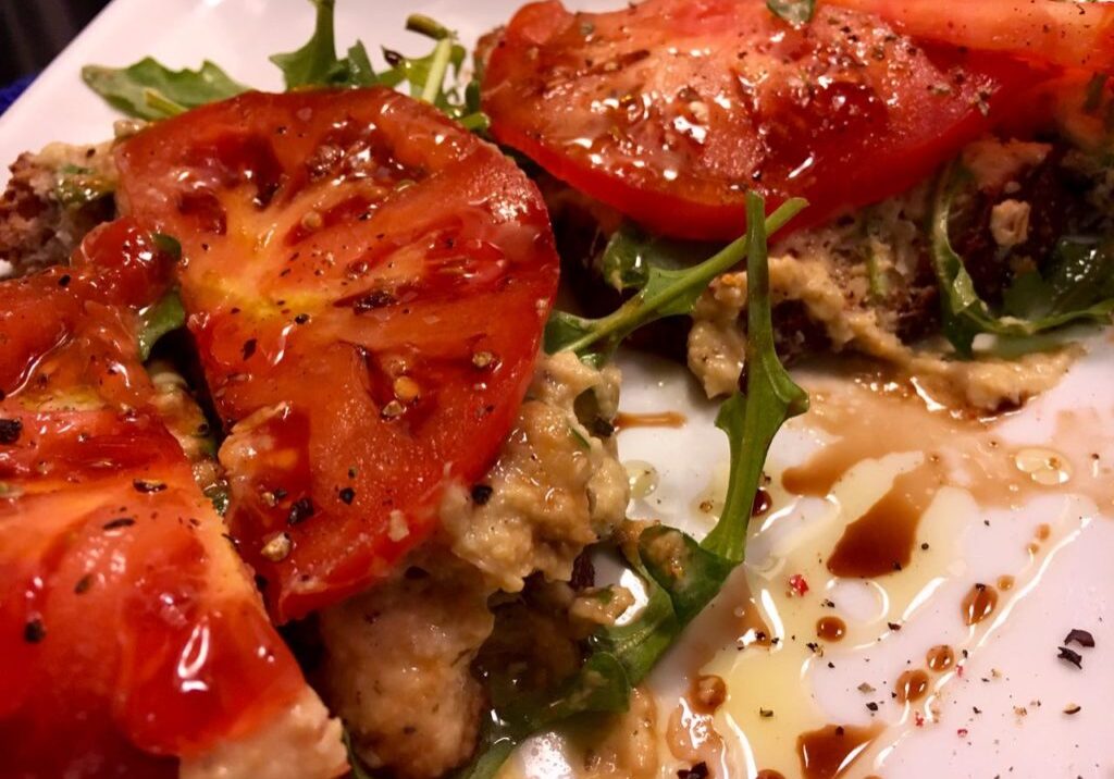 Grilled tomato halves on a bed of greens with a drizzle of balsamic glaze.
