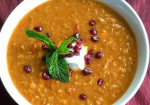 A bowl of lentil soup garnished with mint and pomegranate seeds.