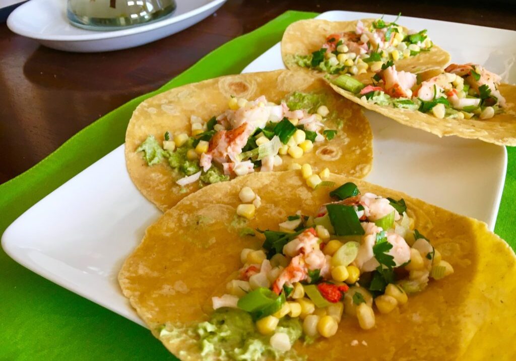 Three tacos filled with corn, vegetables, and herbs on a white plate.