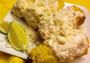 Corn on the cob topped with creamy cheese sauce and a lime wedge.