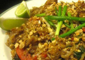 A plate of spicy crab dish garnished with green onions and lime wedges.