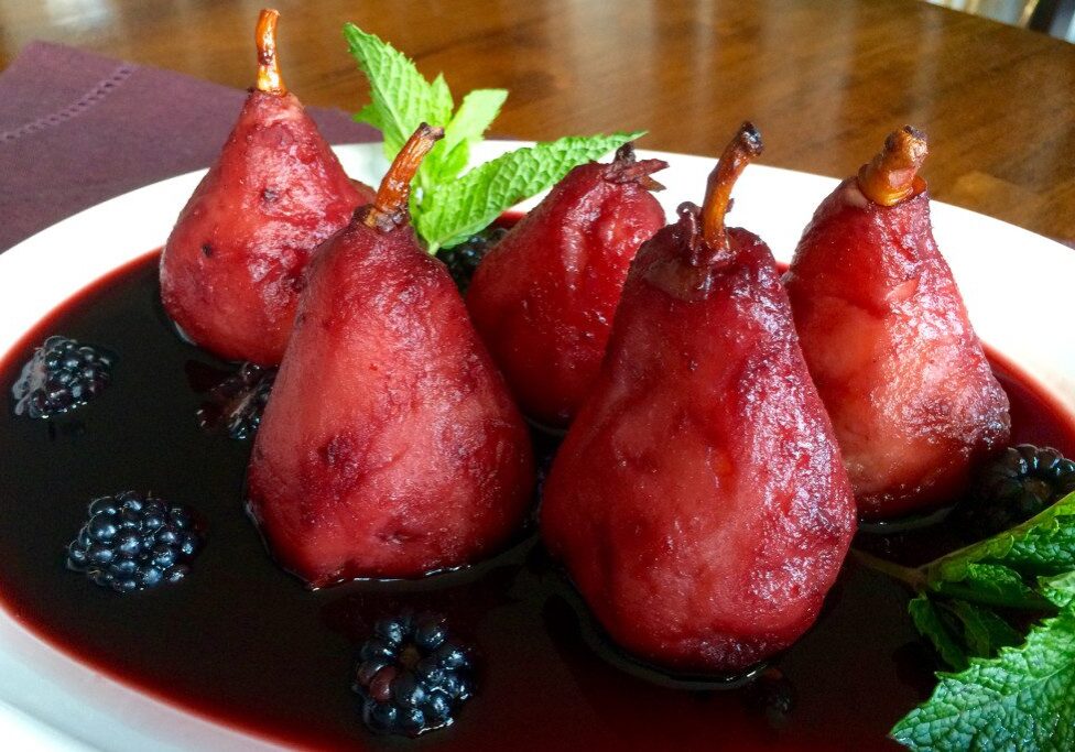 Red wine poached pears garnished with mint leaves on a plate.