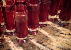 Rows of tall glasses filled with a red beverage on a countertop.