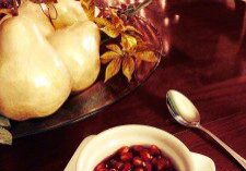 A bowl of pomegranate seeds with decorative gourds in the background.